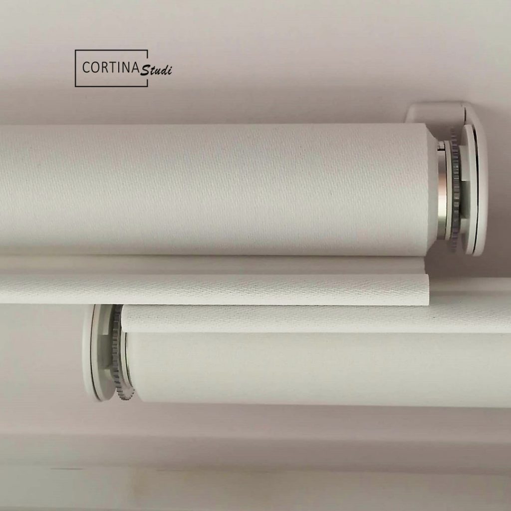 Detalle de estores enrollables de screen con una instalación a medida de CortinaStudi, la mejor tienda de cortinas en Barcelona, los estores están hechos con tejido técnico de screen de bandalux, y son un tipo de cortinatecnica con prestaciones térmicas para proteger los espacios del frio y del calos, la instalación personalizada al techo muestra los estores cruzados para evitar el espacio sin tela entre uno y otro, en CortinaStudi somos especialistas en instalaciones de cortinas a medida profesionales y de calidad