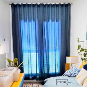 Cortinas azules en una habitación infantil con textiles a medida en forma de cojines y colchas haciendo juego y combinando colores alegres en decoración